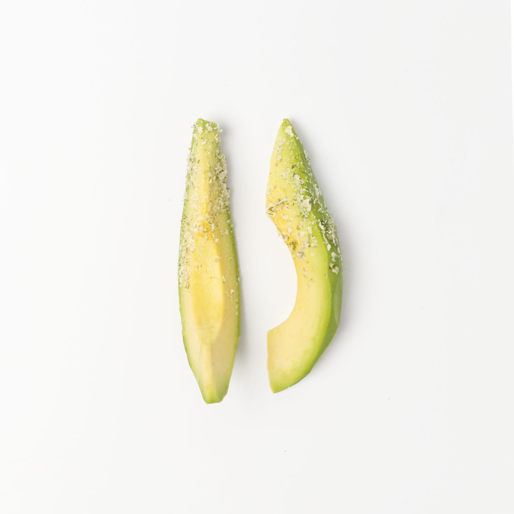 Avocado cut into sticks, sprinkled with pumpkin seed crumbs, on a white background