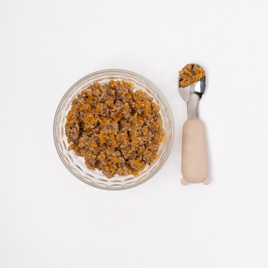 Ground chicken hearts with stewed carrots in a bowl with a spoon beside it on a white background