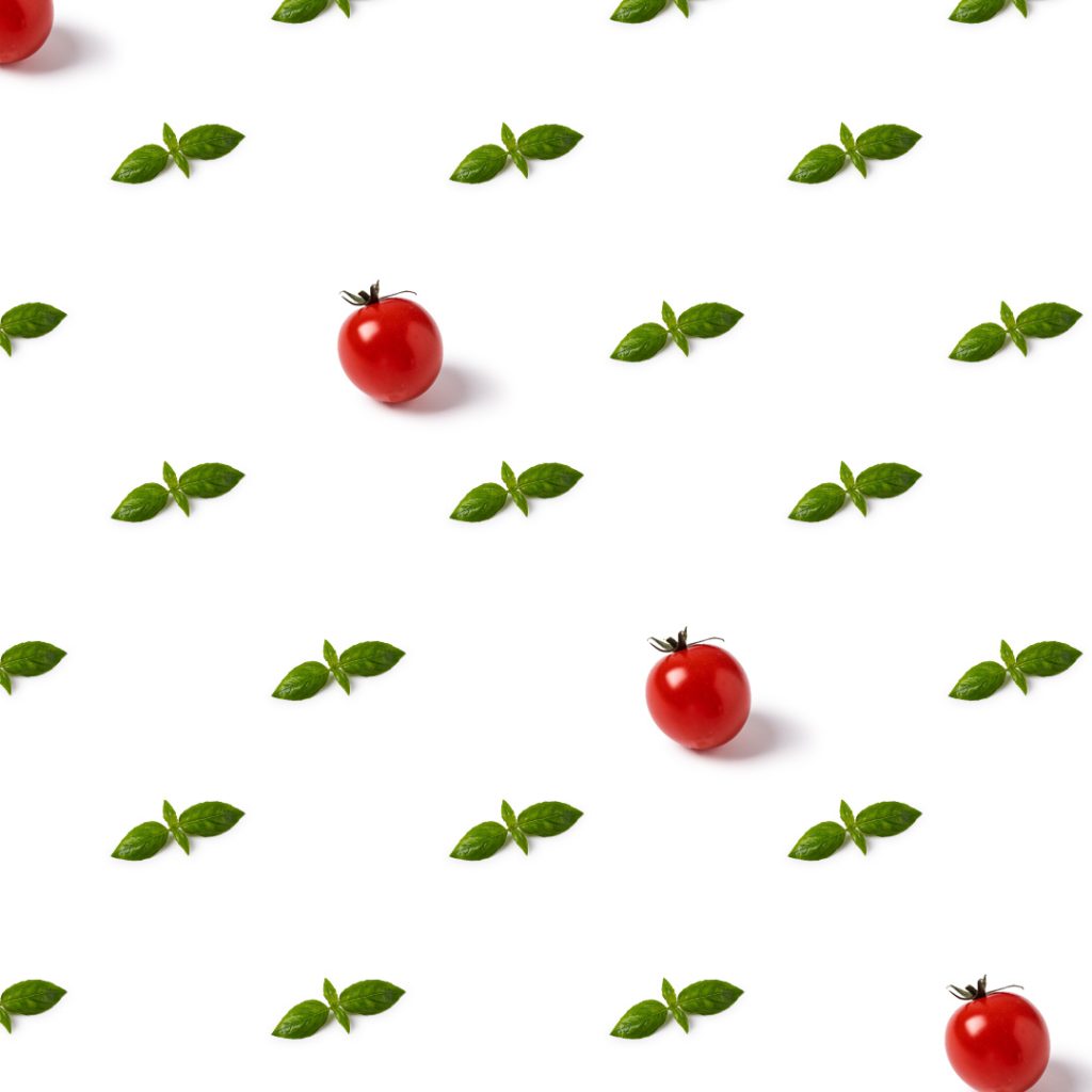 Graphic pattern made of basil leaves and tomatoes on a white background