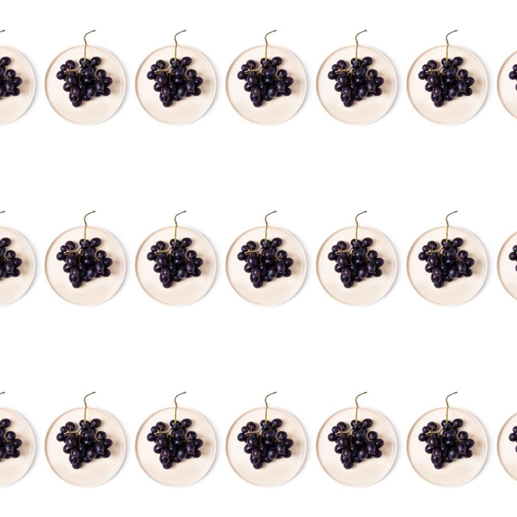 Graphic pattern of parallel lines made of blue grapes on a plate, white background